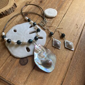 Könnte beinhalten: Ein Halsketten- und Ohrring-Set mit schillernden Abalone-Muschel-Anhängern, dunkelgrünen Perlen und weißen Perlen.