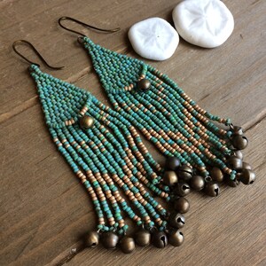 Peut inclure: Une paire de longues boucles d'oreilles en perles de couleur turquoise et or. Les boucles d'oreilles sont ornées d'une frange de petites cloches.