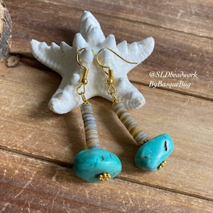 May include: Turquoise and gold earrings with a stack of small, round, white, brown, and yellow beads. The earrings are hanging from a starfish on a wooden surface. The text "@SLDbeadwork ByBasqueBug" is visible in the image.