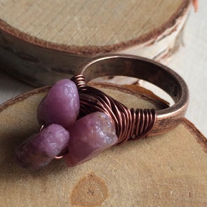 May include: A copper wire wrapped ring with three purple gemstones. The ring is on a wooden surface.