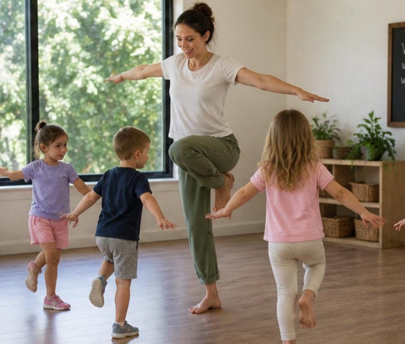May include: A woman and several children are balancing on one leg with arms outstretched. The woman wears a white t-shirt and green pants. The children wear colorful t-shirts and shorts. The scene takes place in a bright room with a large window.