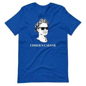 May include: A royal blue t-shirt featuring a white graphic of a bust of a man wearing sunglasses and a laurel wreath. The text "COOLIUS CAESAR" is printed below the graphic.