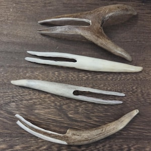 May include: Four individual two-pronged forks carved from natural antler material. Each fork features a unique, organic shape with a smooth, polished finish, displaying varied shades of tan, brown, and off-white tones across their curved surfaces.
