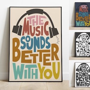 Puede incluir: Un póster colorido con el texto "The Music Sounds Better With You" en una fuente estilizada. El texto está rodeado por un contorno negro de un par de auriculares.