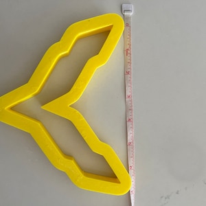 May include: A yellow plastic cookie cutter shaped like a bird with a wingspan of approximately 6 inches.