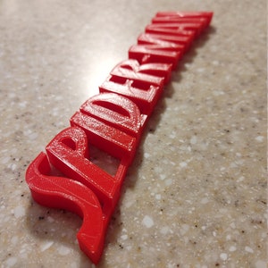 May include: A red 3D printed word "Spiderman" with a slightly curved shape.