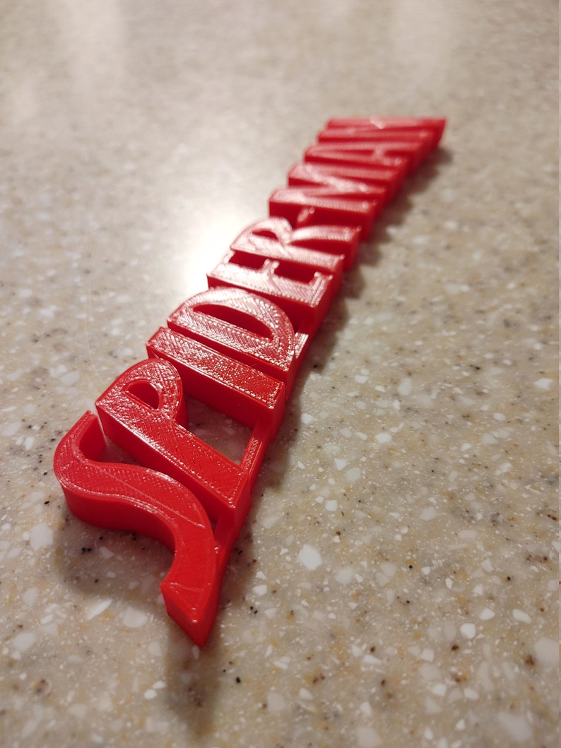 May include: A red 3D printed word "Spiderman" with a slightly curved shape.
