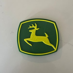 May include: A green and yellow 3D printed logo of a leaping deer. The deer is yellow and the background is green.