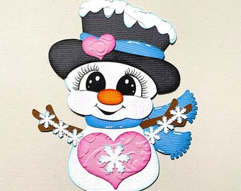 Puede incluir: Un lindo muñeco de nieve con un sombrero de copa negro, una bufanda azul y un corazón rosa con un copo de nieve en el pecho. El muñeco de nieve tiene una cara feliz con ojos grandes y una nariz de zanahoria.