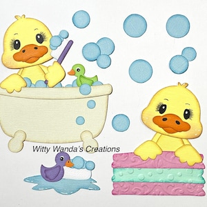 May include: A whimsical illustration features yellow ducklings in a bath-themed setting. One duckling is in a bathtub with bubbles, another is resting on towels, and a third is in a small pool. The image includes the text "Witty Wanda's Creations".