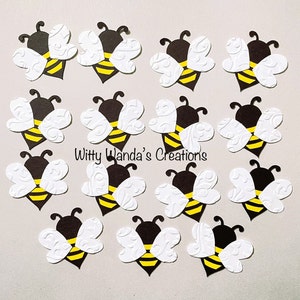 May include: A set of 15 black and white paper bee cutouts with yellow accents. The bees have white wings with a swirl pattern and black bodies with yellow stripes. The text "Witty Wanda's Creations" is printed in black on a white background.