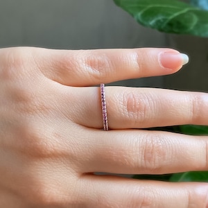 May include: A delicate gold band ring with a row of small pink gemstones.