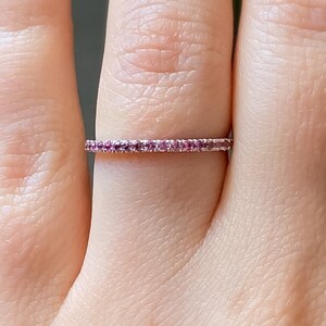 May include: A delicate, thin band ring with a row of small pink gemstones set in a silver band.