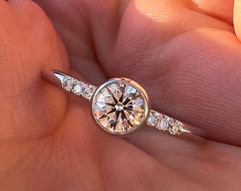 May include: A silver ring with a round, bezel-set diamond and smaller diamonds set in the band.