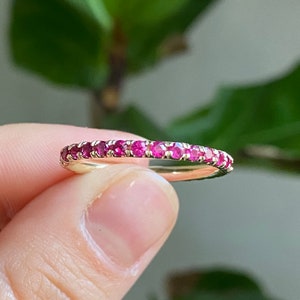 Könnte beinhalten: Ein zarter Goldring mit einer Reihe kleiner, leuchtend rosa Rubin-Steine, die um die gesamte Band gefasst sind.