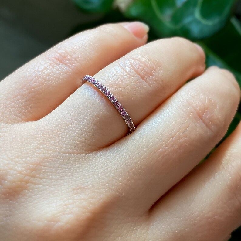 May include: A delicate eternity band ring with a thin band of white metal set with a row of small pink gemstones.