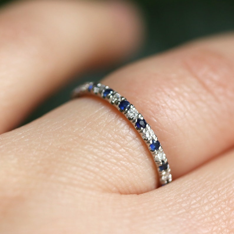 May include: A delicate eternity band ring with alternating blue sapphires and white diamonds set in a silver band.