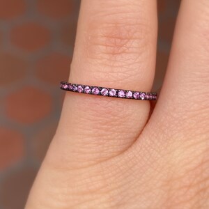 May include: A thin black band ring with a row of small pink gemstones.