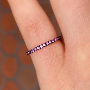 May include: A thin black band ring with a row of small pink gemstones.