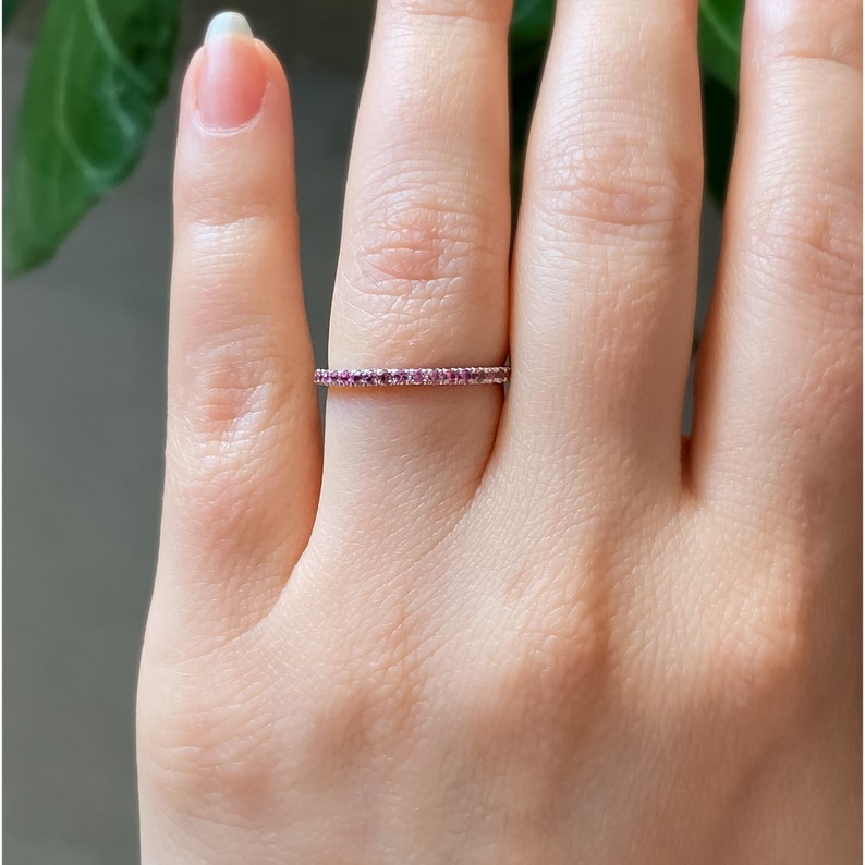May include: A delicate, thin band ring with a row of small pink gemstones set in a silver band.