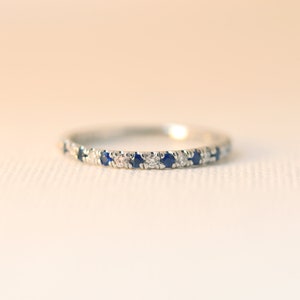 May include: A delicate silver band ring with alternating blue sapphires and white diamonds.