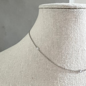 May include: A delicate silver necklace with three small, round, clear gemstones evenly spaced along the chain. The necklace is displayed on a neutral-colored mannequin, showcasing its simple elegance and design.