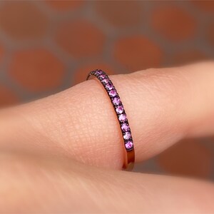 May include: A delicate, thin band ring with a row of small pink gemstones set in a black metal band.