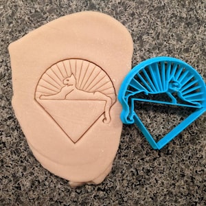May include: Blue plastic cookie cutter shaped like a diamond with a cat and sun design.