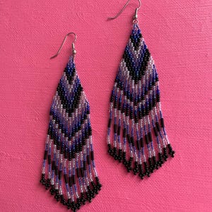 May include: A pair of long, beaded earrings with a chevron pattern in shades of black, purple, and white.