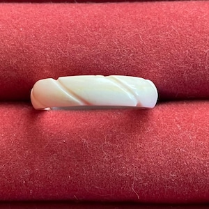 May include: A solid white ring featuring a series of diagonal carved grooves along its outer surface. The band has a smooth, rounded profile and a consistent width throughout, showcasing a clean, uniform appearance with no additional embellishments.