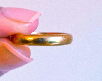 May include: A simple, polished gold band ring with a smooth, rounded surface. The metal has a warm, reflective yellow tone and a consistent, uniform thickness throughout the entire circular shape of the jewelry piece.