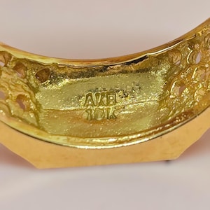 May include: A gold ring featuring a textured, porous surface on the sides and a smooth inner band. The interior of the ring is clearly stamped with the text AKB and 10K, indicating the metal purity and manufacturer mark.