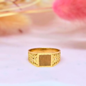 May include: A gold ring featuring a flat, rectangular center plate with a brushed finish. The band is constructed with an intricate, openwork filigree pattern that extends from the central plate around the sides of the ring.