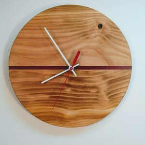 May include: A round wooden clock with a red and white minute and hour hand. The clock face has a thin red stripe across the center.