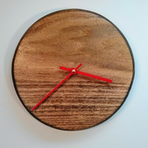 May include: A round wooden clock with red hands. The clock face is made of dark wood with a natural grain pattern.
