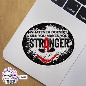 May include: Oval sticker with the text "WHATEVER DOESN'T KILL YOU MAKES YOU STRONGER" in white and red, with a black and white splatter design. The sticker features a red smile and the letter "A".