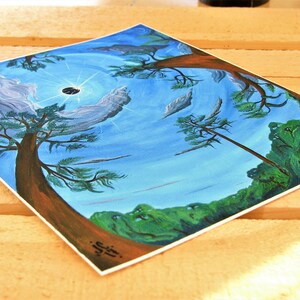 Puede incluir: Una pintura de un cielo azul con nubes blancas y un sol negro. Dos &aacute;rboles est&aacute;n en primer plano, uno a cada lado de la pintura. Los &aacute;rboles son marrones con hojas verdes. La pintura est&aacute; sobre una superficie de madera.