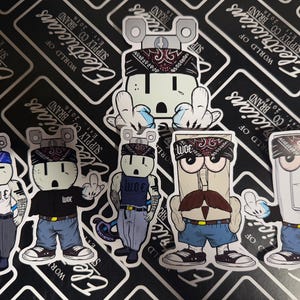 May include: Five colorful stickers featuring cartoon illustrations of electrical outlets and light switches wearing bandanas and clothing. The stickers are printed with the text "W.O.E" and "Electricians Supply Co. Brand Est. 2016 World of Electricians".