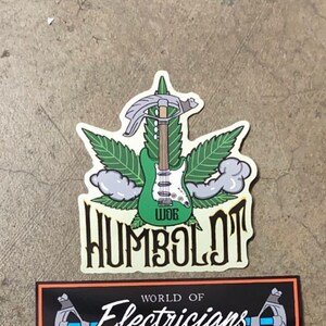 May include: A green and white electric guitar with a marijuana leaf design and the text "Humboldt" in a stylized font. The guitar is topped with a wrench.
