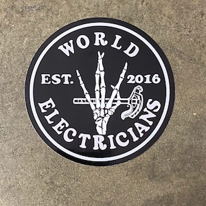 May include: Black and white sticker with a circle design. The circle has the text "WORLD ELECTRICIANS EST. 2016" around the edge. Inside the circle is a skeleton hand holding a wrench.
