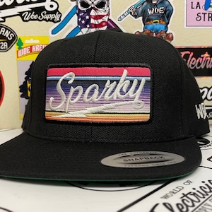 Könnte beinhalten: Schwarze, passformgerechte Baseballkappe mit grünem Schirm, verziert mit einem schwarzen und weißen gestickten 'Sparky'-Patch. Der Patch hat ein Regenbogenstreifen-Design mit einem weißen Blitz. Die Kappe trägt ein schwarzes und weißes 'The Authentic Snapback'-Etikett.