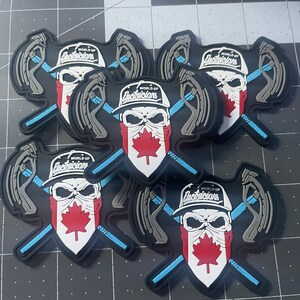 Könnte beinhalten: Fünf schwarze und graue Patches mit einem Totenkopf, der eine weiße Baseballkappe mit dem Text "WORLD OF ELECTRICIANS" trägt. Der Totenkopf trägt ein rot-weißes Bandana mit einem kanadischen Ahornblatt. Der Totenkopf hält zwei gekreuzte Werkzeuge.