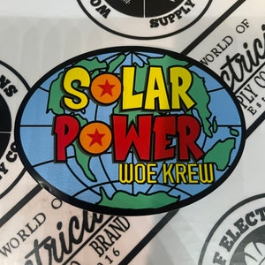 May include: A blue and green circular sticker with a globe design. The text "SOLAR POWER" is in yellow and red letters with a red star on each word. The text "WOE KREW" is in white letters below the globe.