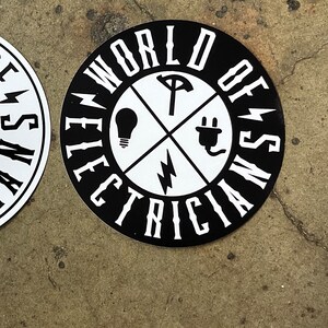 Könnte beinhalten: Schwarz-weißer Aufkleber mit dem Text "World of Electricians" in einem Kreis. Die Mitte des Aufklebers hat ein weißes Kreuz mit einer Glühbirne, einer Steckdose, einem Blitz und einem Schraubenschlüssel.