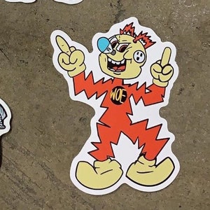 May include: A sticker featuring a cartoon character with a yellow face, red spiky hair, and a blue nose. The character is wearing a red outfit with the word "WOE" on the chest and is pointing with both hands. The sticker has a white border.