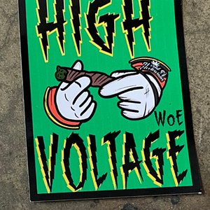 May include: Green sticker with black and yellow text that reads "HIGH VOLTAGE" with a cartoon hand holding a joint and another cartoon hand holding a bag of "Wild Oats Medicinals".