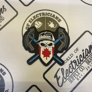 Könnte beinhalten: Ein schwarz-weißes Patch mit einem Schädel, der einen Hut trägt, auf dem "World of Electricians" steht. Der Schädel hält zwei gekreuzte Schraubenschlüssel. Das Patch ist von einem grünen Kreis umgeben, auf dem in weiß "World of Electricians" steht.