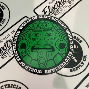 May include: A green and black circular sticker with the text "World of Electricians World of Electricians" around the edge. The center of the sticker features a green stylized face with a lightning bolt above it.