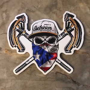 May include: A sticker featuring a skull wearing a baseball cap with the text "World of Electricians." The skull has a bandana with the Puerto Rican flag. Two crossed electrical tools are behind the skull.