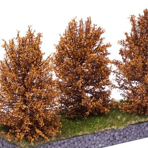 May include: Three miniature trees with brown foliage, set on a green grassy base with a gray stone border. The trees are arranged in a row, with the tallest tree in the center.